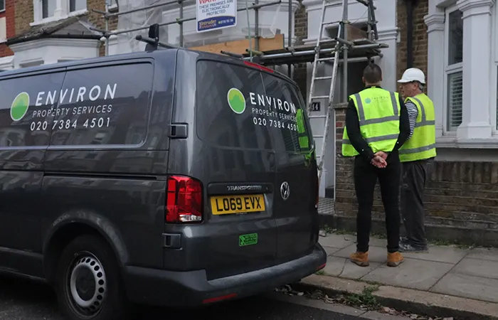 Environ Property Services van parked on street with two workers in high-visibility jackets discussing drainage solutions near a residential building, highlighting professional assistance for subsidence issues.