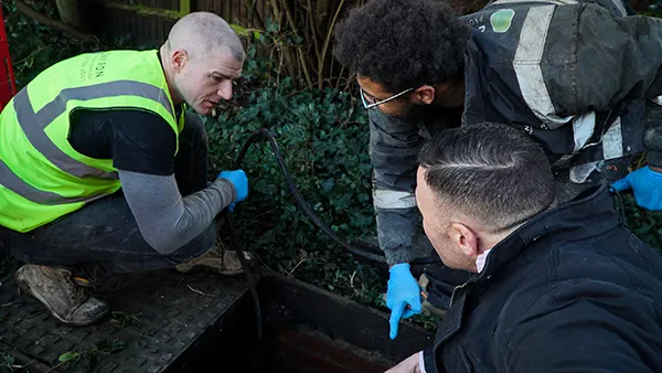 Engineers conducting a CCTV drain survey, discussing drainage issues with a client, surrounded by greenery and equipment.