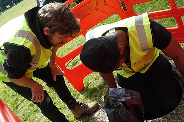 Two drainage engineers in high-visibility vests examining a blockage near an orange safety barrier, demonstrating professional drainage services in action.