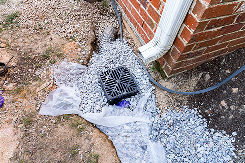 Drainage system components including a drainage grate, gravel, and a downspout, illustrating potential drainage issues relevant to professional services.