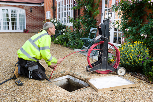 Technician inspecting and clearing a blocked drain using specialized equipment in a residential garden setting.