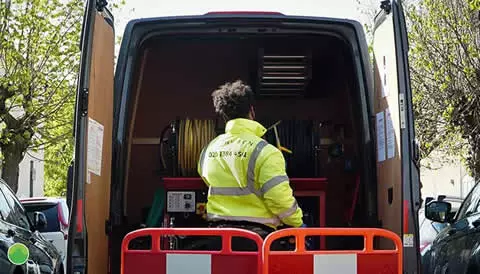 Engineer in high-visibility jacket working from the back of a van equipped with drainage tools and hoses, emphasizing emergency drain services for stadiums and event spaces.