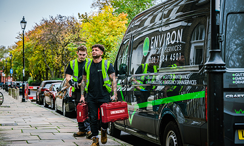 Two drainage engineers from Environ Drainage Services carrying emergency toolkits near their service van in a London street, showcasing readiness for urgent drainage issues.