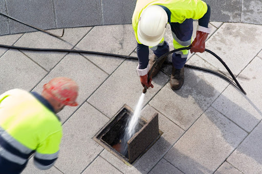 Two workers in high-visibility clothing performing drain cleaning, using high-pressure water jetting on a drainage system in London.